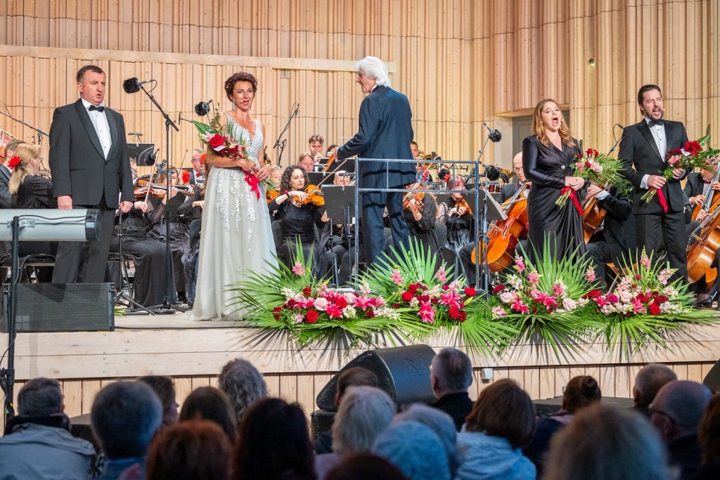 Liepājas vasaras Operas galā koncerts. Uz skatuves operdziedātāja baltā kleitā, diriģents un simfoniskā orķestra mūziķi
