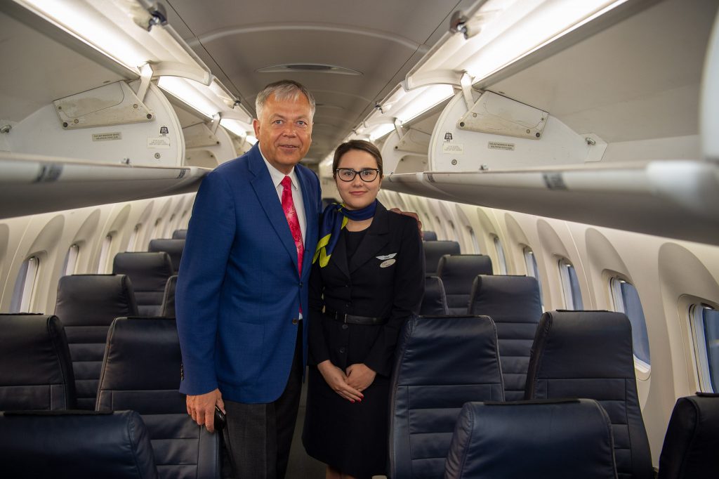 Liepājas domes priekšsēdētājs Uldis Sesks un airBaltic stjuarte lidmašīnas salonā.
