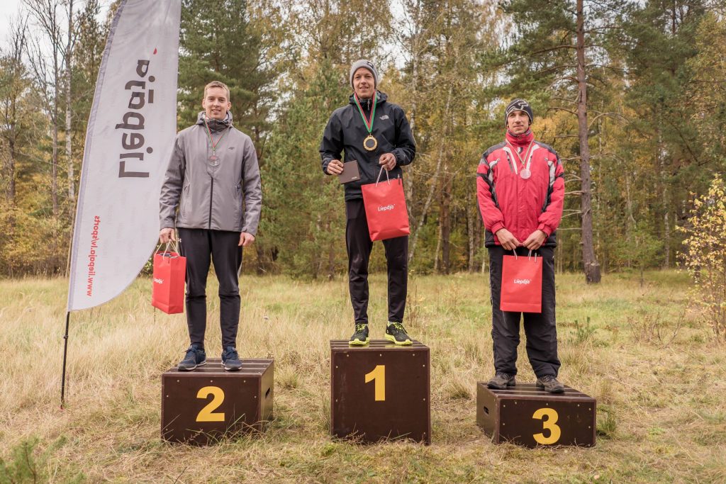 Trīs vīrieši uz goda pjedestāla orientēšanas sacensībās