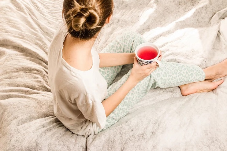 Meitene ar tējas krūzi sēž gultā